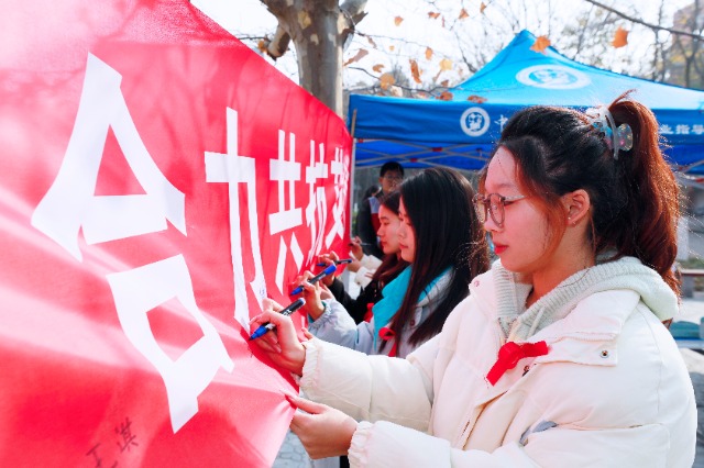 20231127中國石油大學(xué)（華東）青年學(xué)子在合力共抗艾滋的條幅上簽字，表達抗擊艾滋病的決心和信心  .jpg